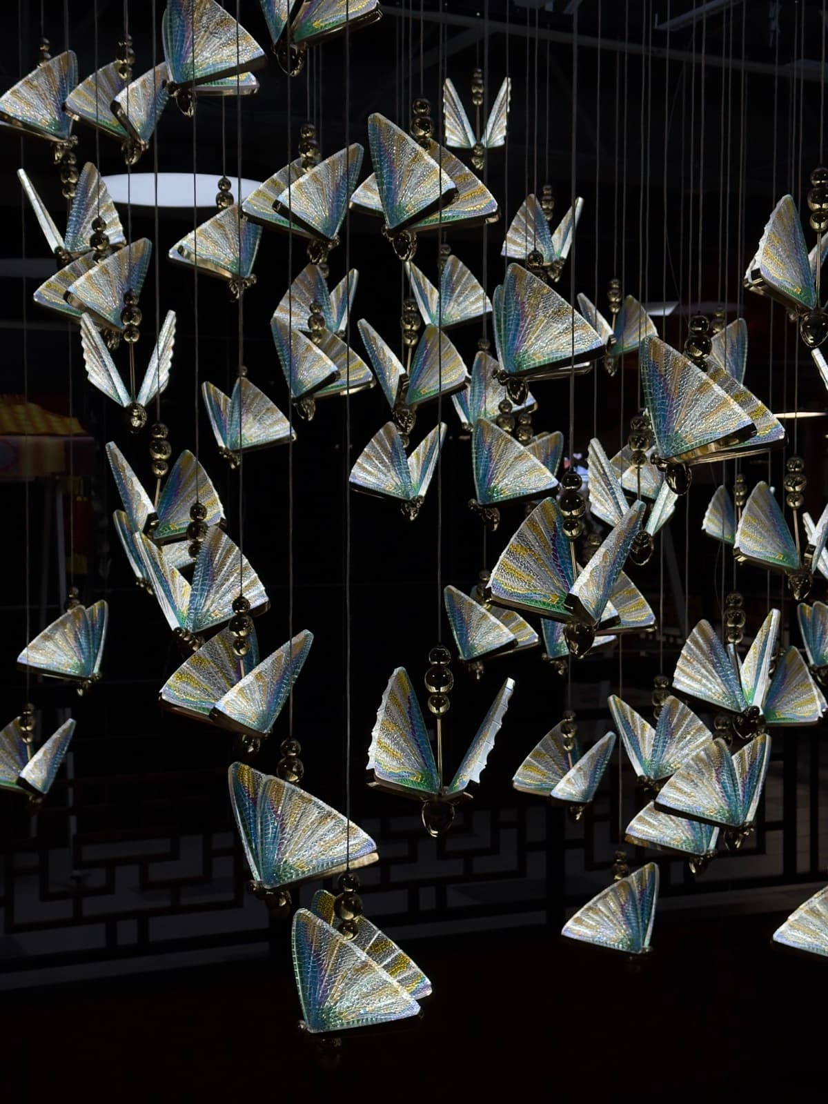 An installation of iridescent glass butterfly ornaments suspended on wires against a dark background.